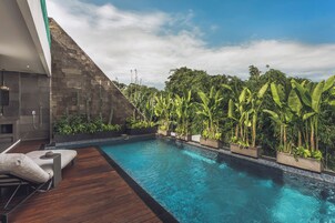 A modern pool area with a wooden deck, a built-in seating area, and lush tropical plants.