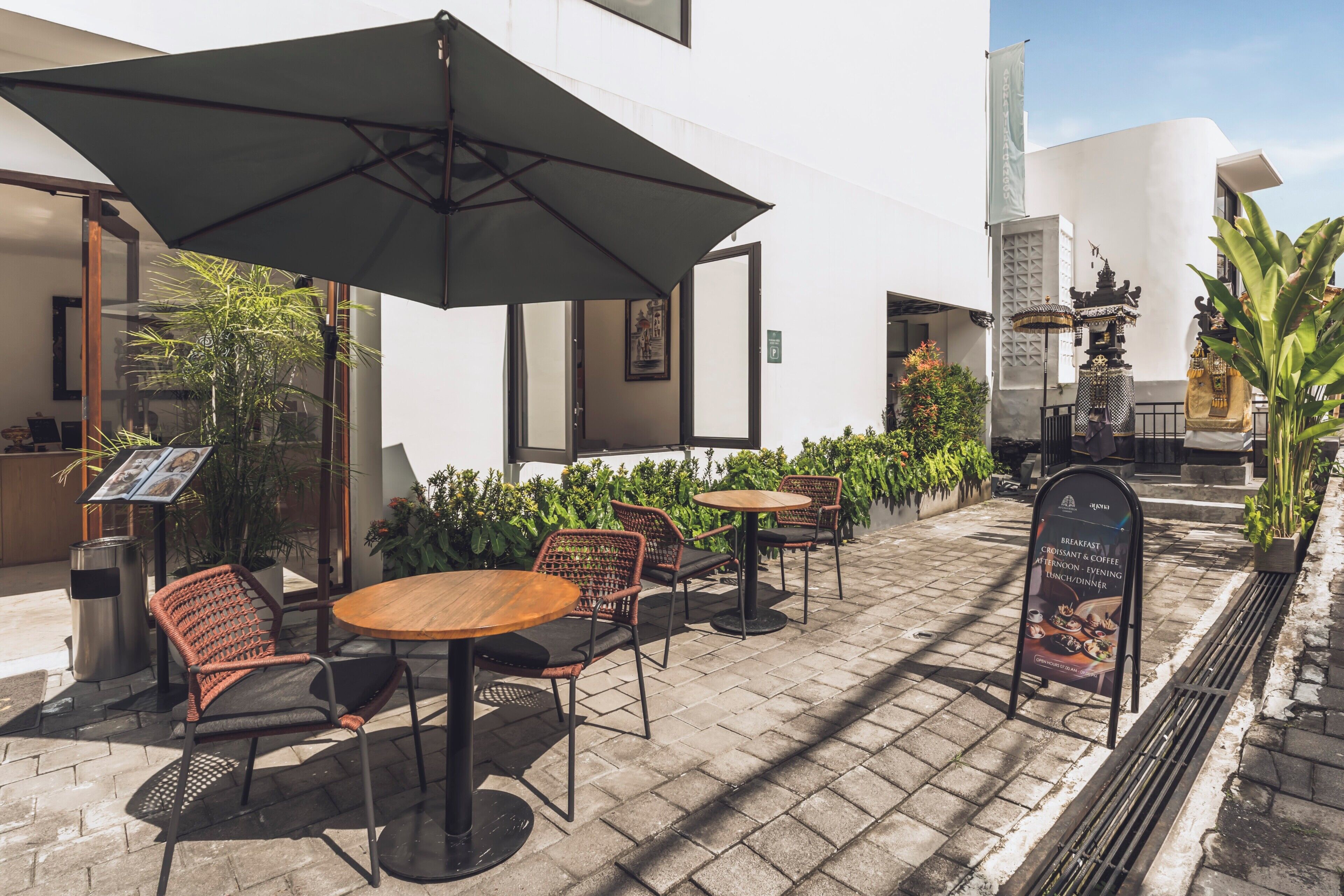 An outdoor seating area with tables and chairs, umbrellas, and a signboard.