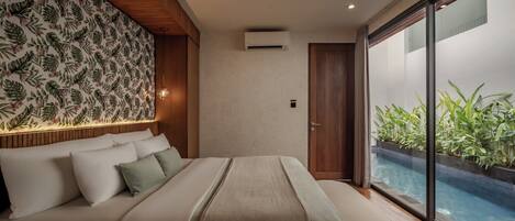 A bedroom with a bed, a wooden headboard, a wall with a leaf pattern, a sliding door to a balcony, and a view of a swimming pool.