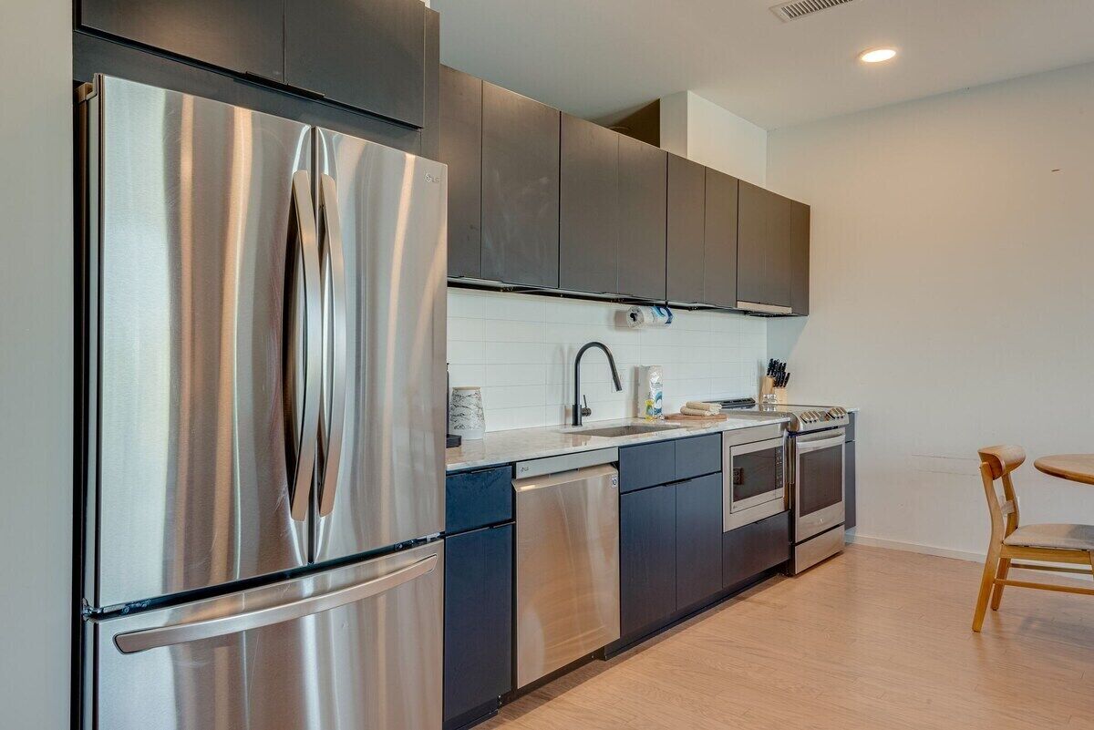 A modern kitchen with stainless steel appliances, dark cabinetry, and a wooden dining table.