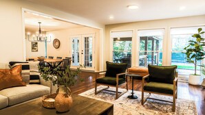 A spacious living room with a large window, a dining area, and a cozy seating arrangement. - Private Estate | Sleeps 35 | 9 Bed 9.5 Bath | 2 Homes | Theater | Pond | Sport Court | Hot Tub | Sauna (Ravenna)