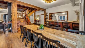 A spacious dining area with a wooden table and chairs, a staircase with exposed beams, and a kitchen in the background. - Private Estate | Sleeps 35 | 9 Bed 9.5 Bath | 2 Homes | Theater | Pond | Sport Court | Hot Tub | Sauna (Ravenna)