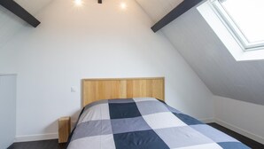 A bedroom with a sloped ceiling, a skylight, a wooden headboard, and a checkered bedspread. - Modern house in the heart of Green Périgord with pets allowed (Preyssac-d'Excideuil)