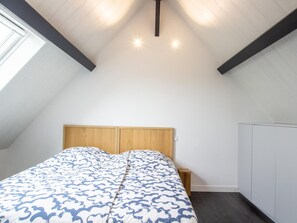 A bedroom with a bed, wooden headboard, bedside table, wardrobe, and sloped ceiling with skylight.