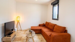 A modern living room with a flat-screen TV, a glass coffee table, an orange sofa, and a floor lamp. - Modern house in the heart of Green Périgord with pets allowed (Preyssac-d'Excideuil)