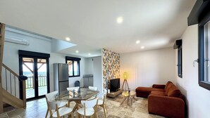 A modern living space with a glass dining table, a sofa, a TV, and a staircase leading to an outdoor area. - Modern house in the heart of Green Périgord with pets allowed (Preyssac-d'Excideuil)