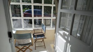Une pièce avec une grande fenêtre, une chaise en bois, une petite table et une porte.