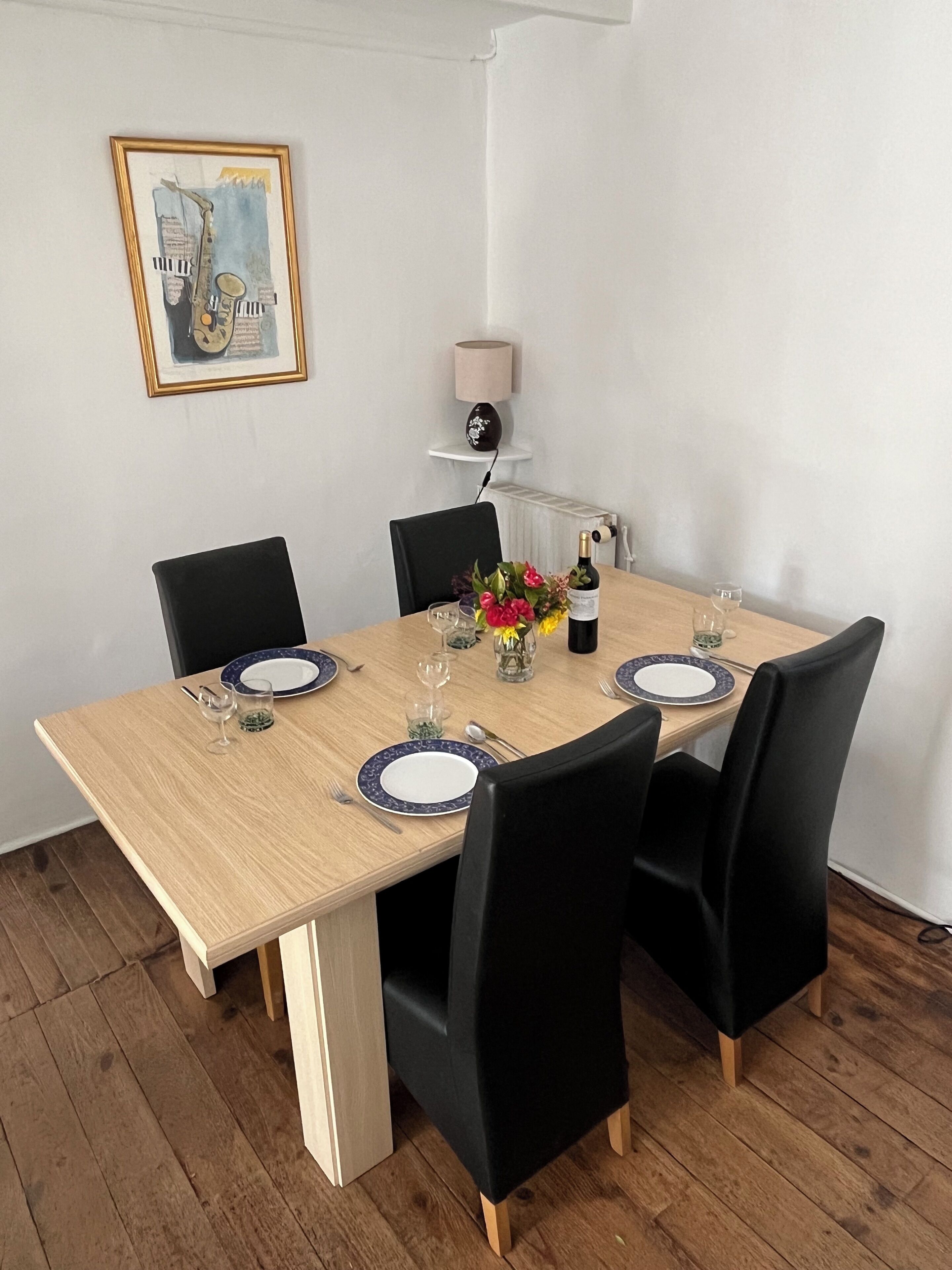 A dining table with black chairs, white plates, and a vase of flowers.