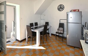 Compact kitchen with a stainless steel refrigerator and dining area, featuring a checkered floor pattern and a clock on the wall.