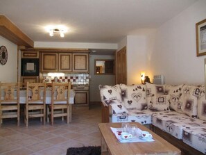 Uma sala de estar acolhedora com sofá, mesa de jantar com cadeiras e cozinha com armários de madeira e painel atrás do fogão.