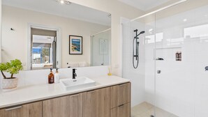 A modern bathroom with a large mirror, a sink, a shower, and a potted plant.