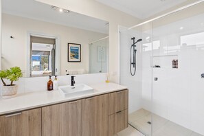 A modern bathroom with a large mirror, a sink, a shower, and a potted plant.