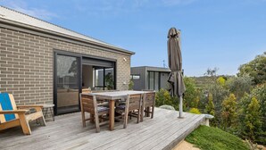A modern house with a deck, a dining table, and outdoor furniture.