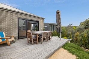 A modern house with a deck, a dining table, and outdoor furniture.