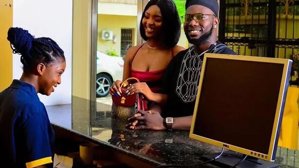 A reception desk with a computer monitor, a chandelier, and a window with a view of the outside. - TD RESIDENCE INN (Ijebu Ode)