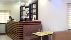 A reception area with a counter, a seating area with a sofa and a table, and a decorative wall with a crown symbol. - TD RESIDENCE INN (Ijebu Ode)