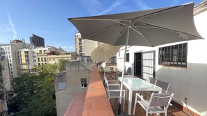 An outdoor terrace with a table and chairs, a large umbrella, and a view of the cityscape. - Cozy attic penthouse in center of BCN. Sun, views, quiet... close to main spots. (Barcelona)