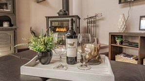 Un salon chaleureux avec une cheminée, un plateau sur lequel se trouvent une bouteille de vin, des verres et une plante en pot.