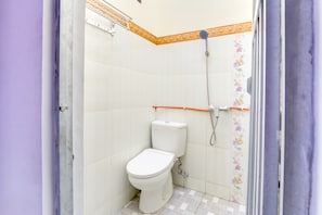Et lille badeværelse med toilet, brusebad og flisegulv.