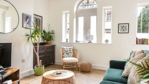 A living room with a green sofa, a wicker coffee table, a wicker chair, a television, a bookshelf, and a large mirror. - Seaward (Lyme Regis)