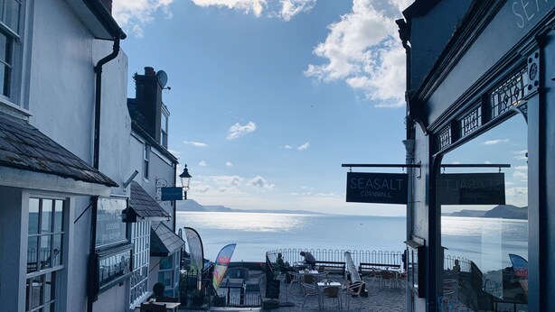 A cobblestone street with outdoor seating, a sign for 'SEASALT CORNWALL', and a view of the sea. - Seaward (Lyme Regis)