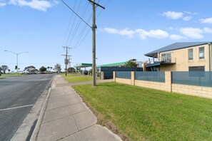 A street with a sidewalk, a gas station, and a building with a fenced area. - Bliss on the Bay - Upstairs and Games Room (Rye)