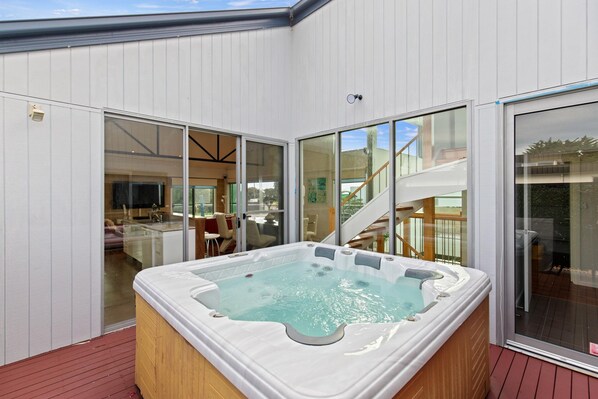 Un bain à remous sur une terrasse en bois, avec une porte vitrée donnant sur une pièce où se trouve un escalier.