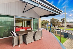 A covered outdoor area with a dining table and chairs, a red sofa, and a large window.