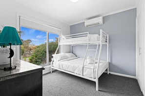 Habitación con literas, escritorio, lámpara, ventanas amplias y aire acondicionado.