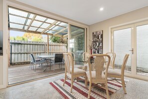 Un comedor con mesa y sillas de vidrio, cercado con valla de madera, y vistas al exterior.