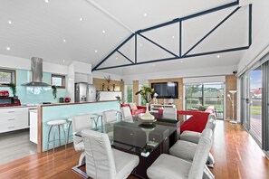 A modern kitchen with a central island, a dining area with a glass table, and a living space with a TV.