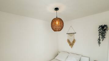 A minimalist bedroom with a single bed, a hanging light fixture, a wall-mounted plant, and a small bedside table with a lamp.