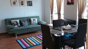 Una sala de estar moderna con un sofá verde, almohadones coloridos, un tapete a rayas y una mesa de comedor con sillas.