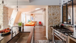 A modern kitchen with a central island, stainless steel appliances, and a stone accent wall. - Soulful Fusion, by Veeve (Paris)