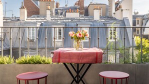 A rooftop terrace with a table set for two, a vase of flowers, and a view of the cityscape. - Soulful Fusion, by Veeve (Paris)