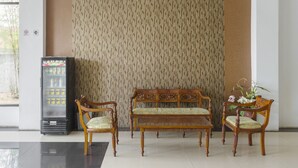 A lobby with a patterned wall, a vending machine, and three wooden chairs and a bench. - OYO 3343 Sunrise Hotel (Banjarbaru)