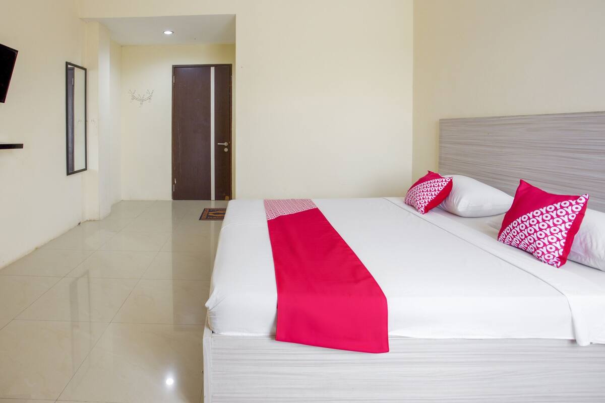 Ein Hotelzimmer mit einem grossen Bett, weisser Bettwäsche und roten Akzenten.