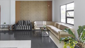 A modern living room with a striped sofa, a beige sofa, a glass coffee table, and a large window. - OYO 3343 Sunrise Hotel (Banjarbaru)