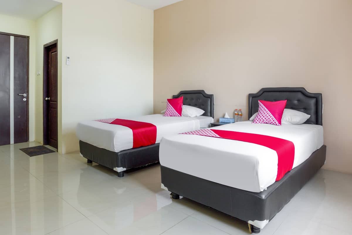 Ein Hotelzimmer mit zwei Betten, jeweils mit schwarzem Kopfteil und weißer Bettwäsche, und einem roten Zierkissen.