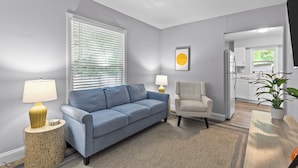Una sala de estar con un sofá azul, un sillón color beige y una mesa de centro. Hay dos lámparas sobre mesitas auxiliares, un cuadro en la pared y una planta en maceta sobre la mesa de centro.