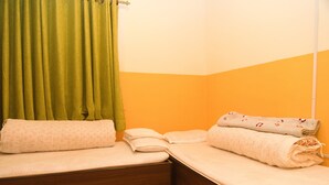 Ein kleines Zimmer mit einem Einzelbett, Holzboden, einem grünen Vorhang und einer weißen Wand mit orangenem unteren Bereich.