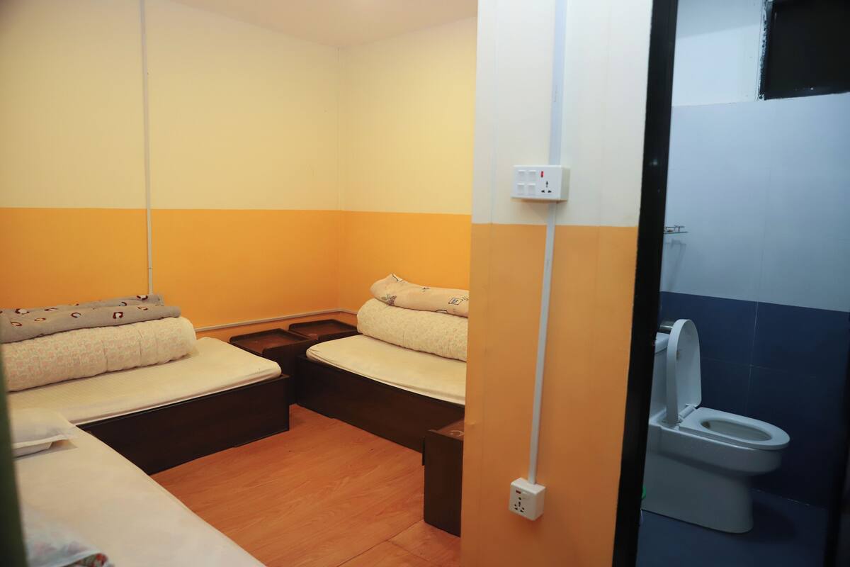 A small, compact room with two beds, a toilet, and a wall socket.