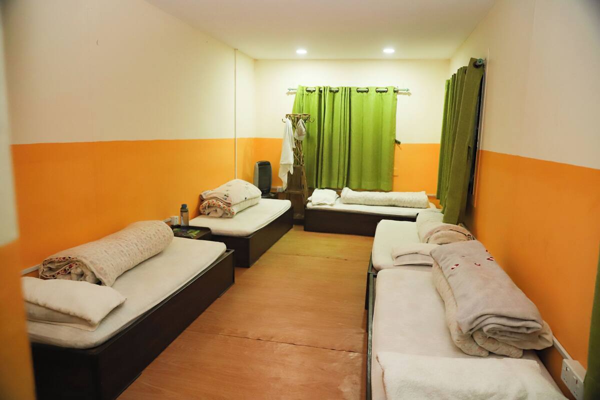 A hotel room with two single beds, a small sofa, a bedside table, and a green curtain.