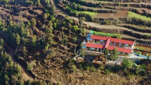 Ein mehrstöckiges Gebäude mit rotem Dach, umgeben von terrassenförmig angelegten Feldern und vereinzelter Vegetation.