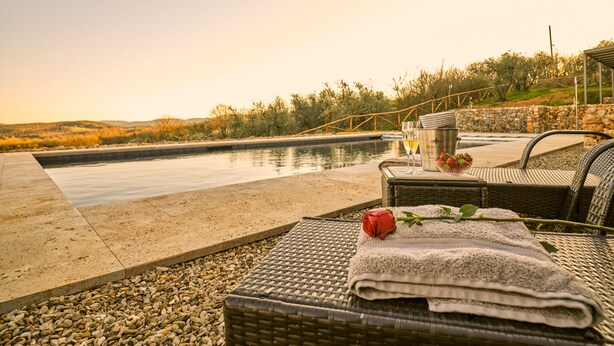 Zona junto a la piscina con mobiliario de mimbre, una rosa y un balde con vasos.
