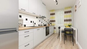 A modern kitchen with white cabinets, a wooden countertop, and a dining area with a white table and black chairs. - Sunny Apartment | 2 Bedrooms, Balcony and Air Conditioning (Warszawa)