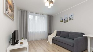 A modern living room with a grey sofa, a white coffee table, and a TV on a white stand. - Sunny Apartment | 2 Bedrooms, Balcony and Air Conditioning (Warszawa)
