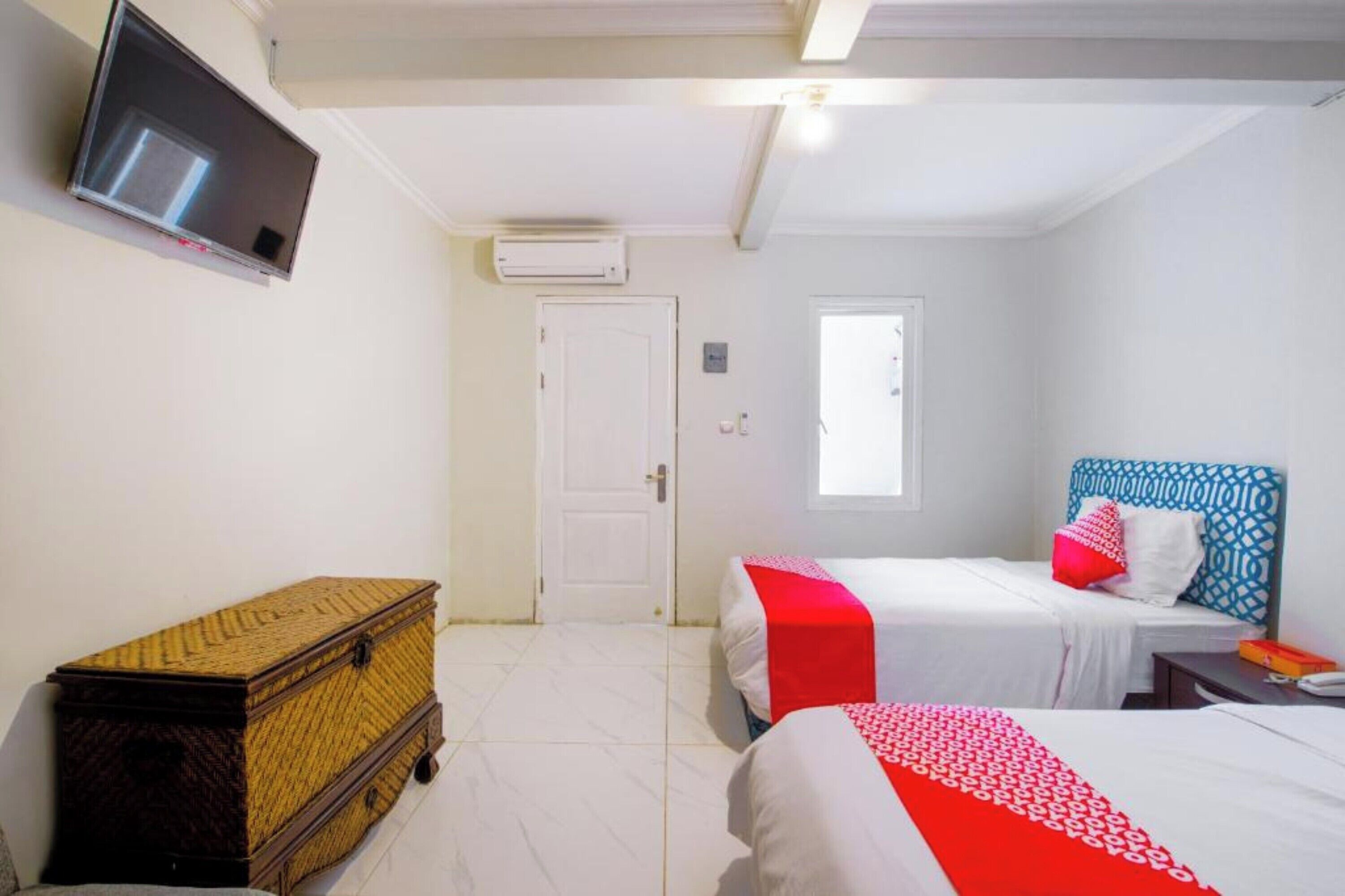 A room with two beds, a television, a wardrobe, and an air conditioning unit.