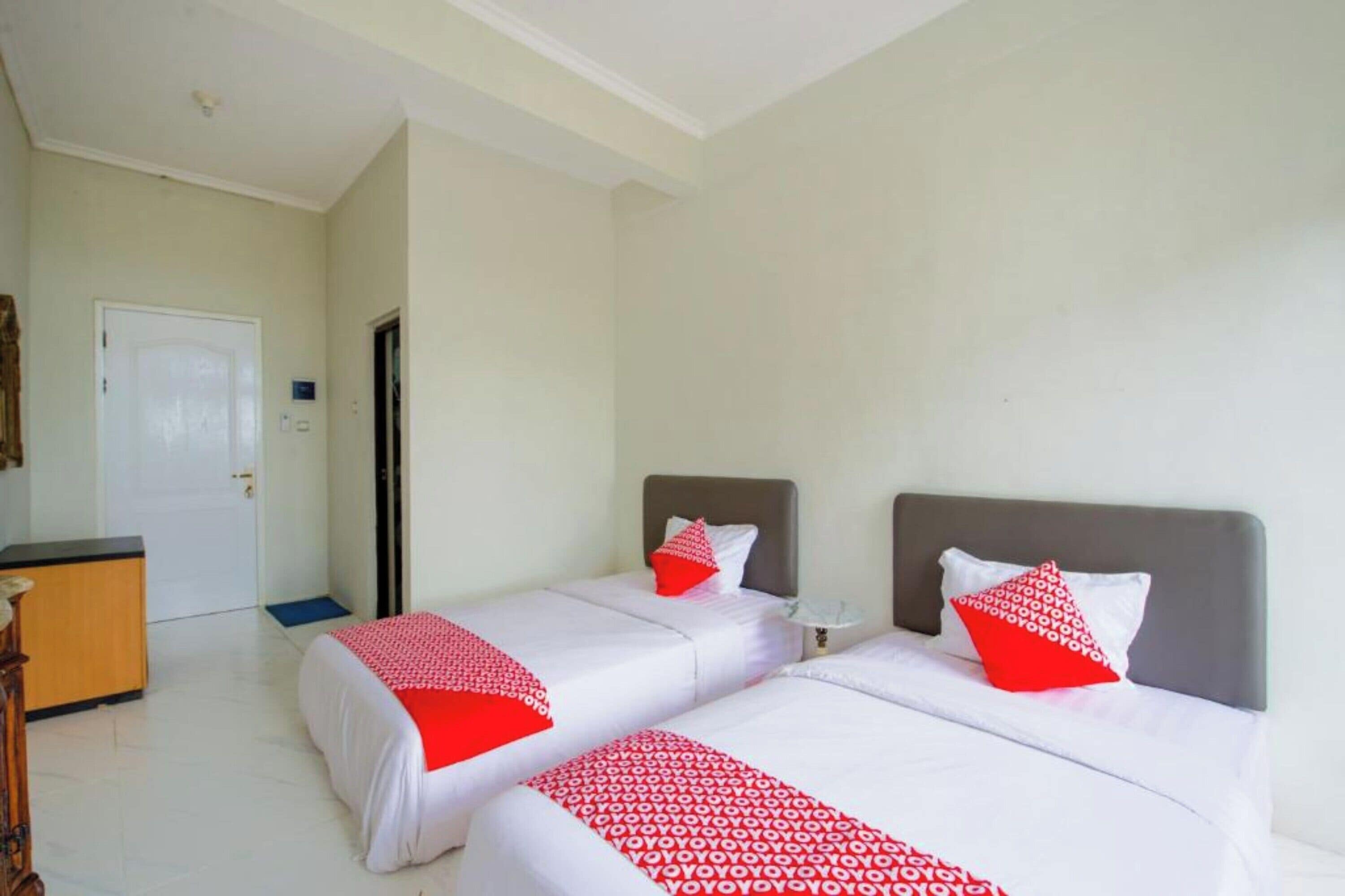 Une chambre d’hôtel avec deux lits, chacun recouvert d’une couvre-lit à motifs rouges et blancs, une petite table de chevet et une commode.