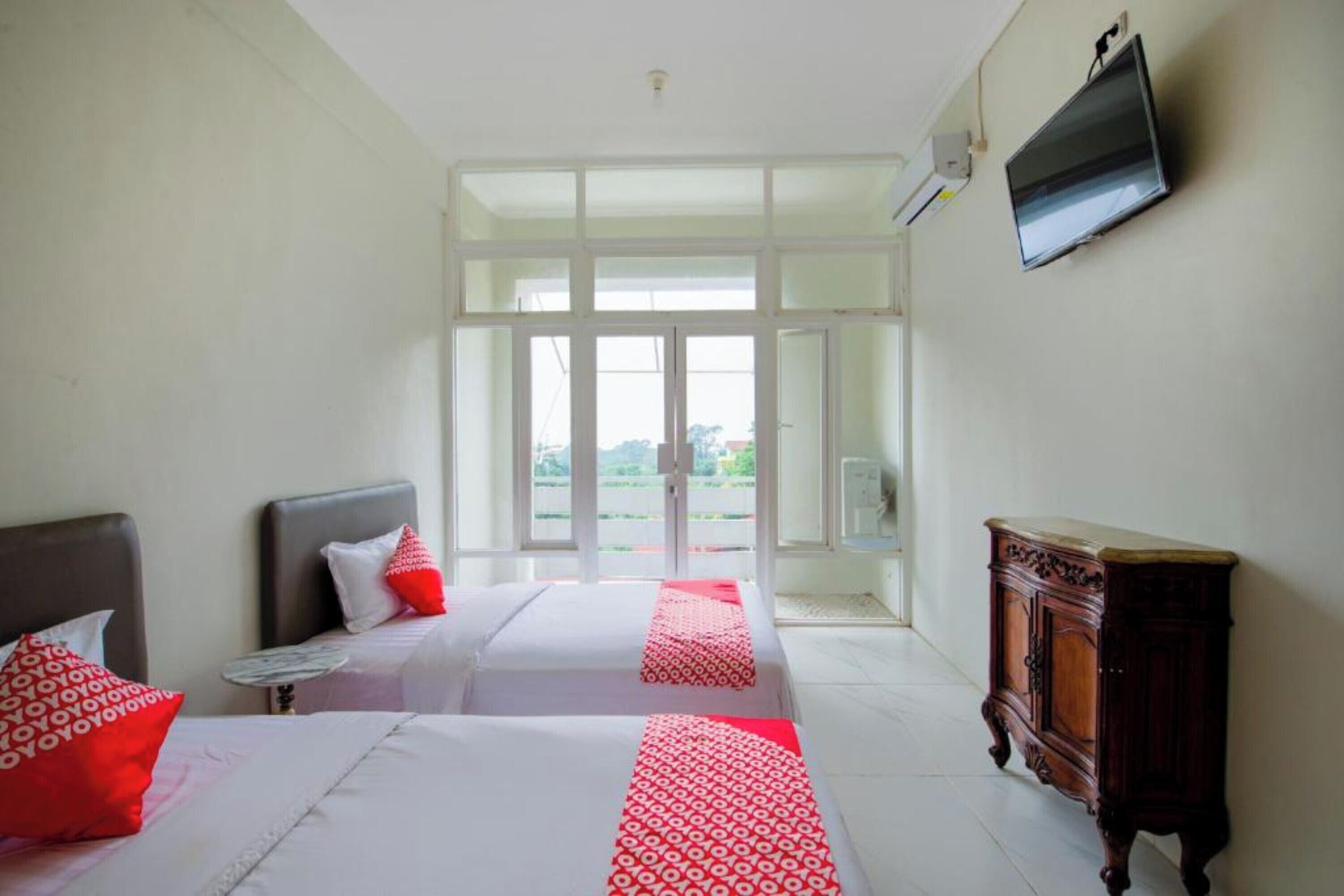Habitación de hotel con dos camas, una mesita, un armario de madera y un televisor montado en la pared.